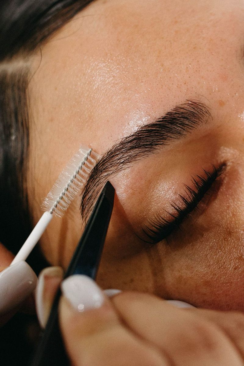 Brow shaping treatment in progress with brush and tweezers